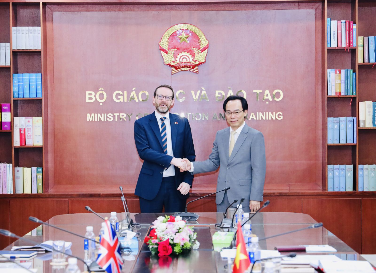 Two men shaking hands in front of a table  Description automatically generated
